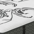 A close-up of a mattress showing its white quilted top with a black abstract scroll pattern and a dark gray textured side panel.